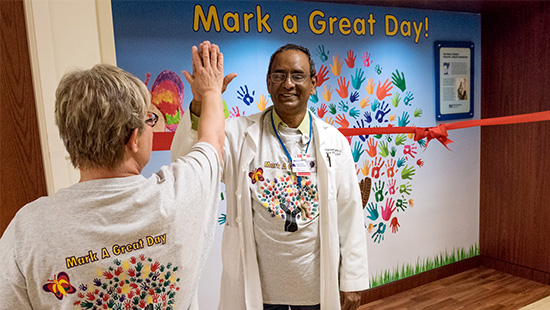 Pediatricians high-five in front of a mural reading 'Mark a Great Day'